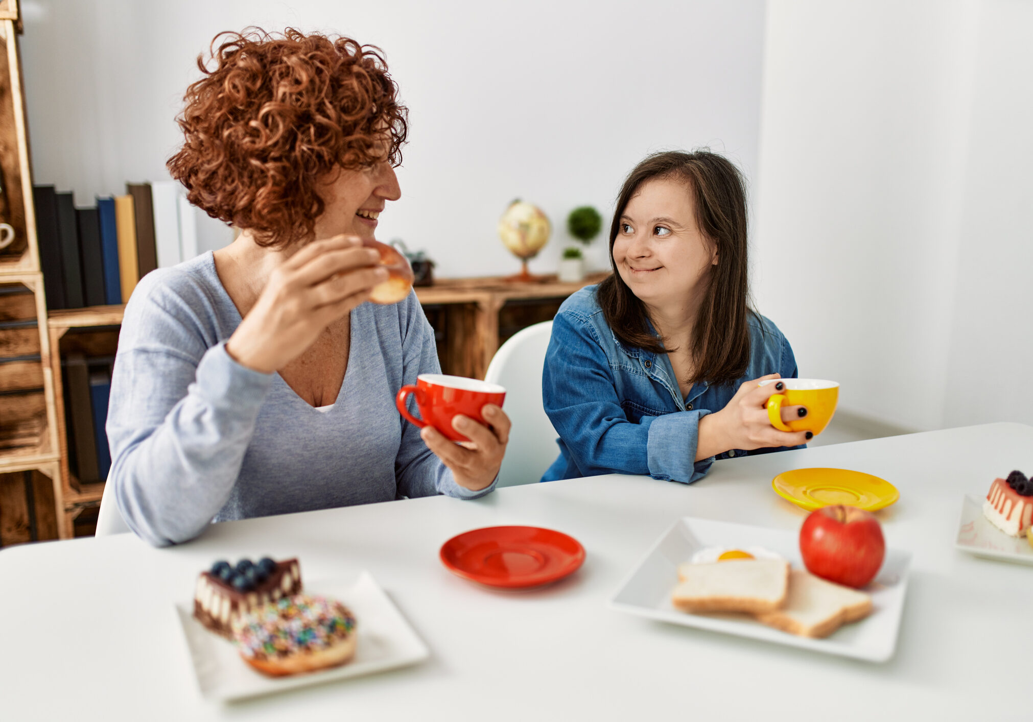 Mature mother and down syndrome daughter having coffee and lunch at home