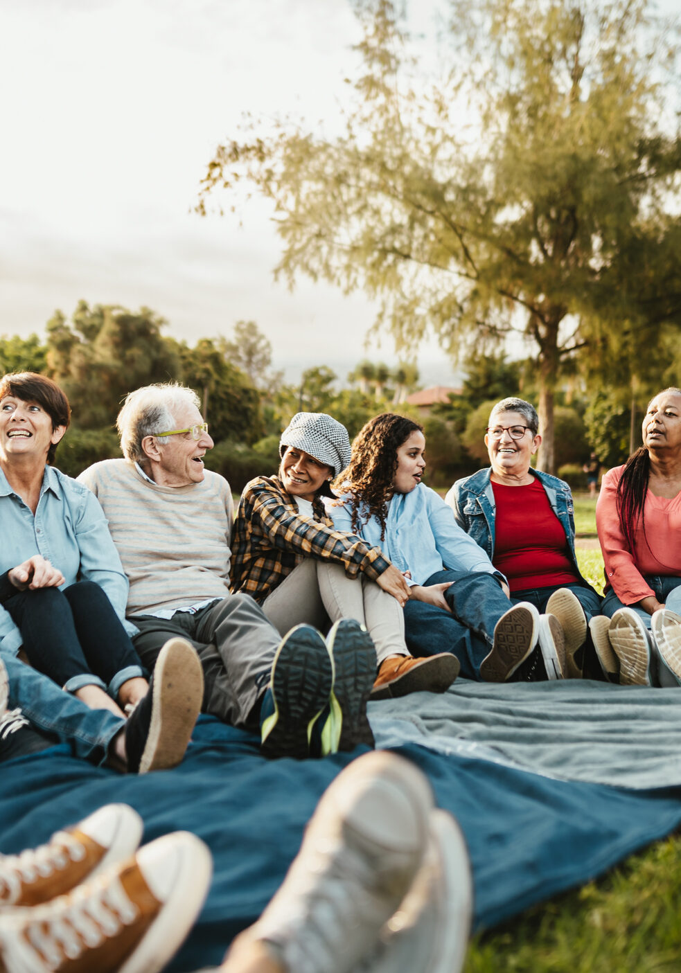 Happy multi generational people having fun sitting on grass in a public park - Diversity and friendship concept