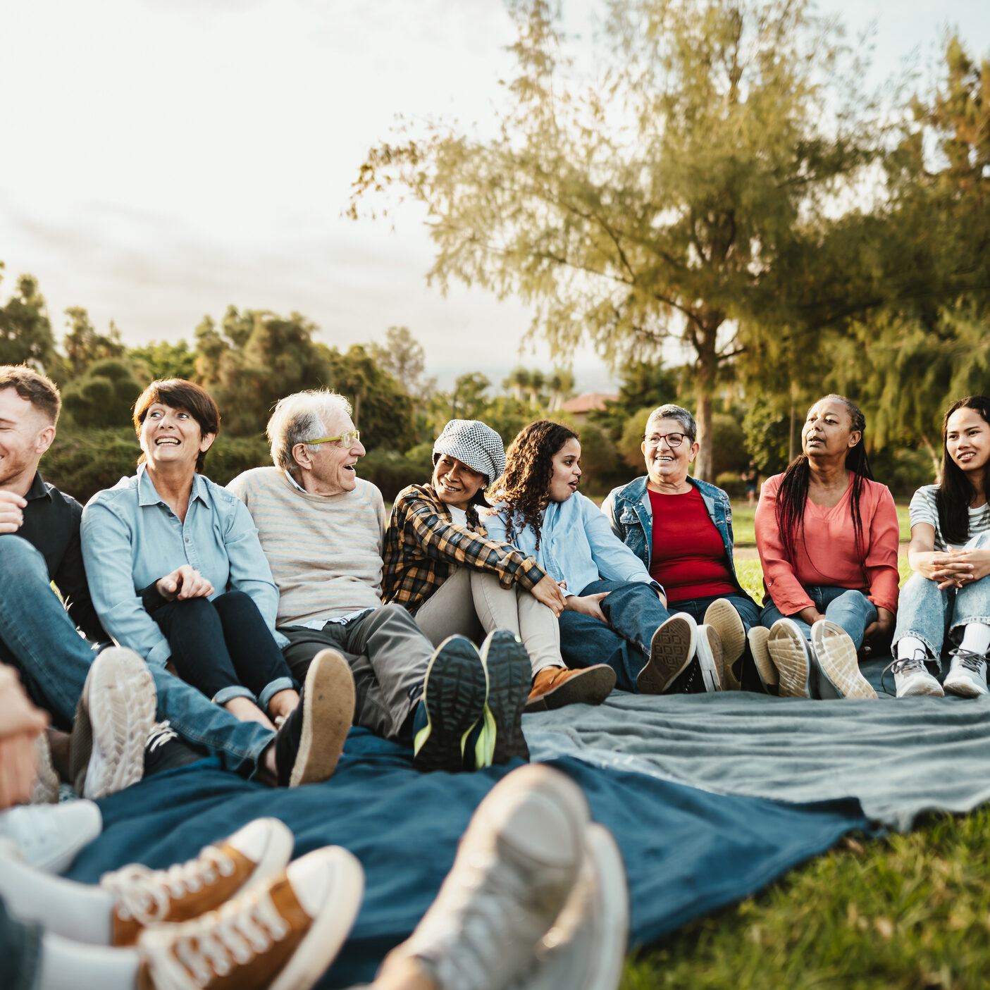 Happy multi generational people having fun sitting on grass in a public park - Diversity and friendship concept